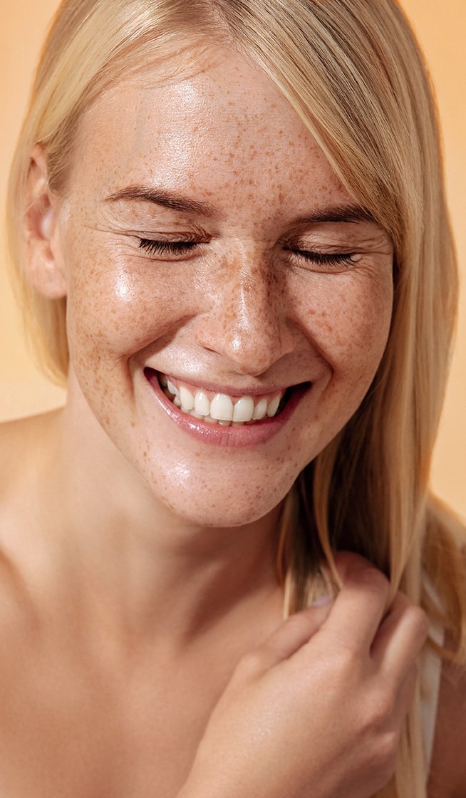Lächelnde, blonde Frau mit schöner Haut vor orangefarbenem Hintergrund