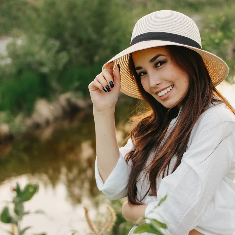 lächelnde Frau an einem Fluss mit einem Hut auf dem Kopf